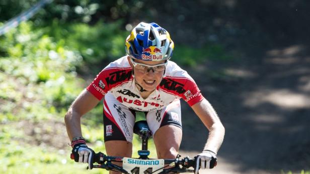 Eine Mountainbikerin mit Helm und Sportbekleidung fährt eine Strecke entlang.