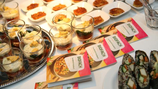Ein Tisch mit verschiedenen Speisen, darunter Sushi, Gemüse-Desserts im Glas und BIOFACH Kochbücher.