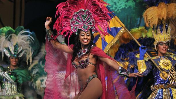 Eine Tänzerin in einem farbenprächtigen Federkostüm tritt auf einer Bühne auf.