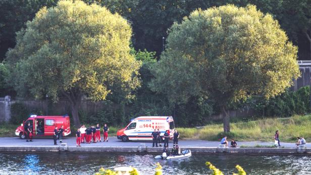 Rettungskräfte und Krankenwagen stehen an einem Flussufer, während ein Boot zu Wasser gelassen wird.