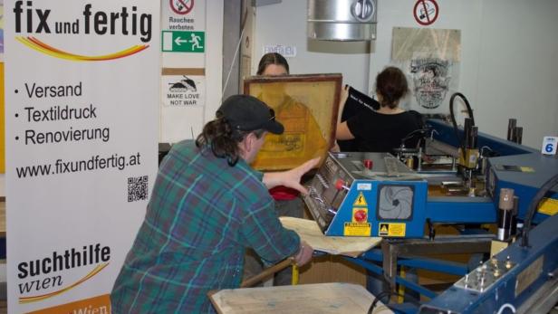 Mitarbeiter bedrucken Textilien in einer Werkstatt von „fix und fertig“ in Wien.
