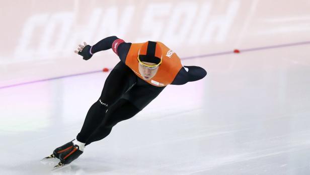 Ein Eisschnellläufer in oranger Wettkampfkleidung auf einer Eisbahn.