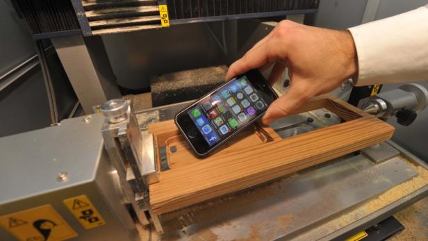 Ein iPhone wird in eine Holzvorrichtung auf einer Werkbank eingesetzt.