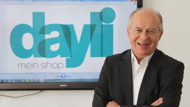 Ein lächelnder Mann im Anzug steht vor einem Bildschirm mit dem Logo „dayli mein shop“.