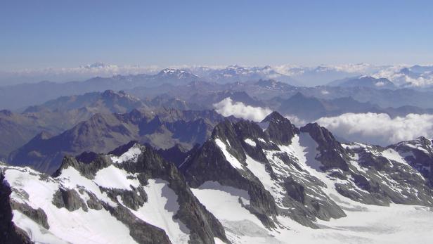 Eine weite Berglandschaft mit schneebedeckten Gipfeln unter einem blauen Himmel.