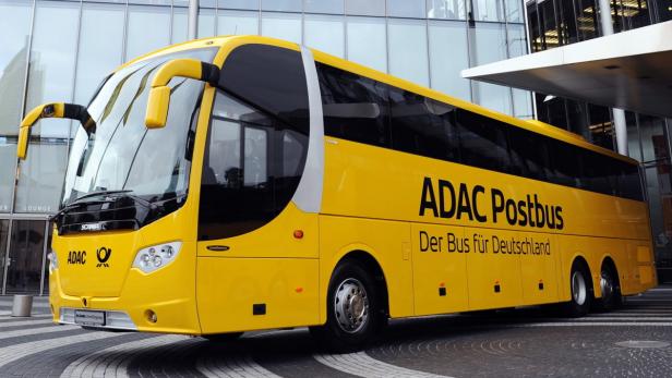Ein gelber ADAC Postbus vor einem modernen Gebäude.