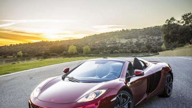 Ein roter McLaren-Sportwagen steht auf einer Landstraße bei Sonnenuntergang.