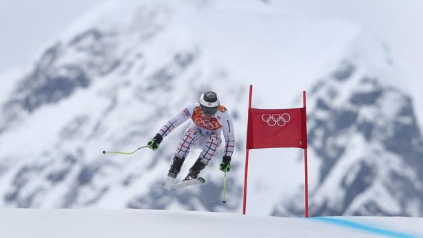 Ein Skifahrer springt während eines Rennens vor einer verschneiten Bergkulisse.