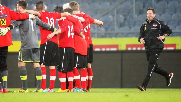 Eine Gruppe Fußballspieler umarmt sich, während ein Trainer am Spielfeldrand entlangläuft.