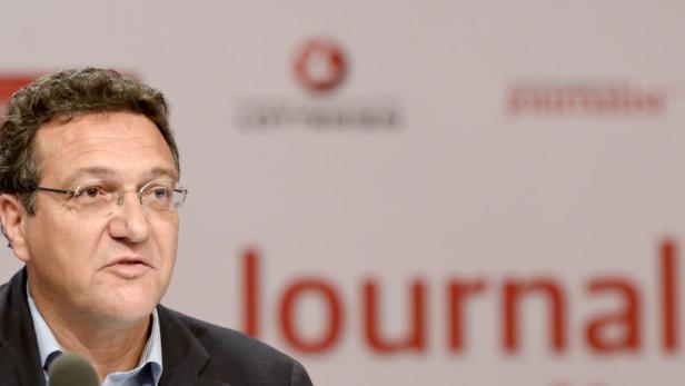 Ein Mann mit Brille spricht vor einem Mikrofon auf einer Pressekonferenz.