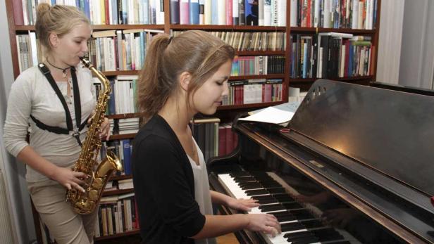 Zwei junge Frauen musizieren; eine spielt Klavier, die andere Saxophon.