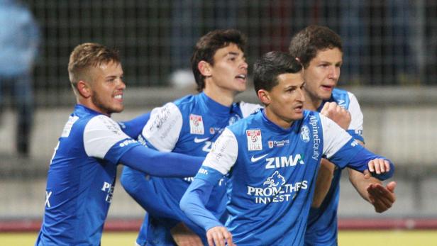 Vier Fußballspieler in blauen Trikots feiern gemeinsam.