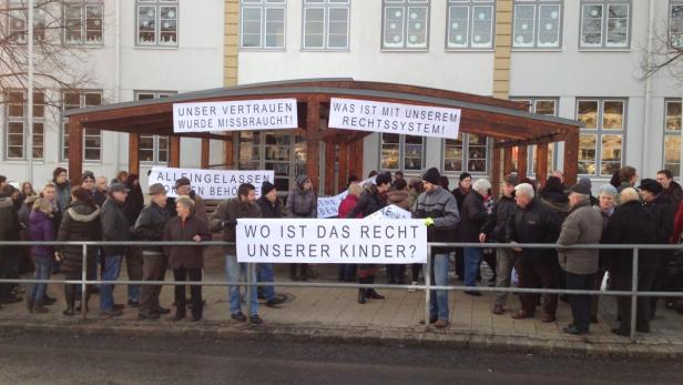 Eine Menschenmenge demonstriert mit Schildern vor einem Gebäude.
