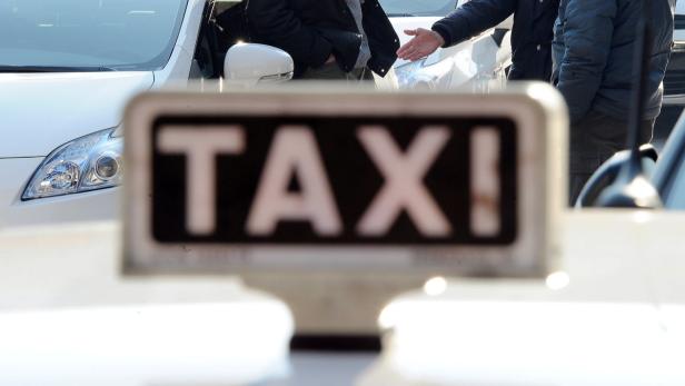 Ein Taxischild vor einem weißen Auto mit zwei Männern im Hintergrund.