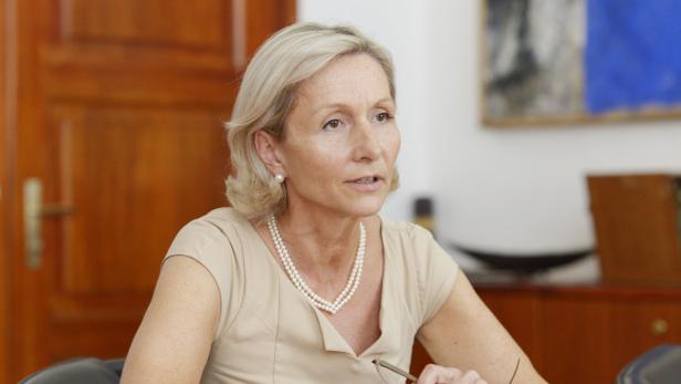 Eine blonde Frau mit Perlenkette sitzt an einem Tisch.