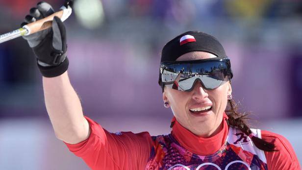 Eine Langläuferin mit polnischer Flagge auf der Mütze jubelt mit erhobenem Stock.