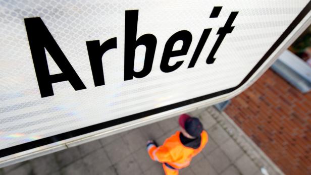 Ein Schild mit der Aufschrift „Arbeit“ und ein Arbeiter im Hintergrund.