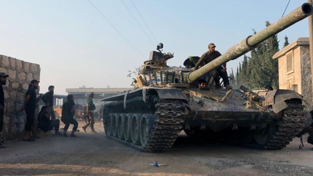 Ein Panzer steht auf einer Straße, umgeben von einer Gruppe von Männern.