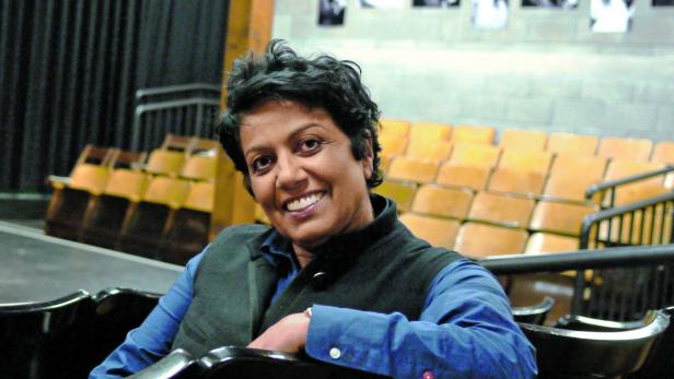 Eine lächelnde Frau sitzt in einem Theatersaal.