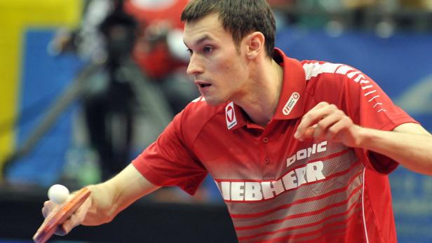 Ein Tischtennisspieler in rotem Trikot schlägt den Ball.