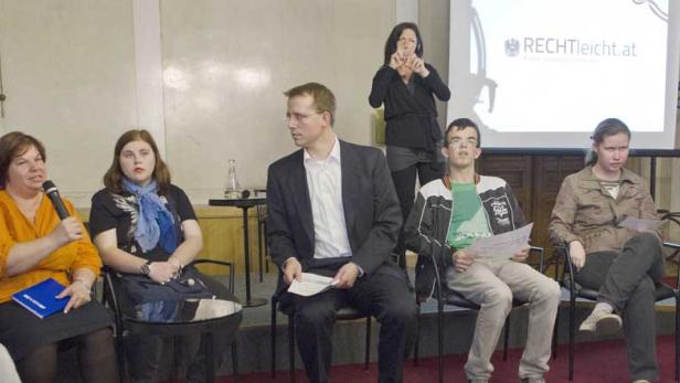 Eine Gruppe von Menschen sitzt auf einer Bühne während einer Präsentation von RECHTleicht.at.