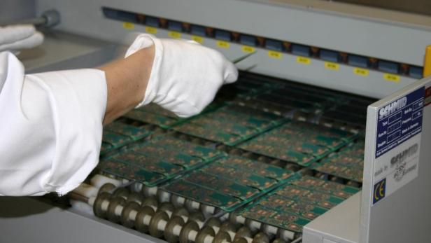 Eine Hand mit Handschuh hantiert mit einer Pinzette an Leiterplatten in einer Fertigungsanlage von Schmid Maschinenbau.