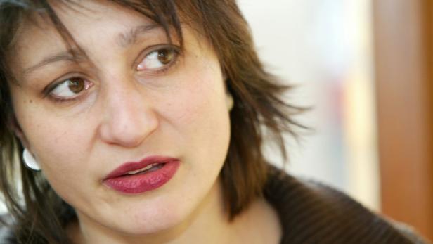 Eine Frau mit braunen Haaren und dunklem Lippenstift schaut zur Seite.