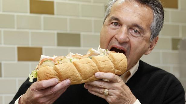Ein Mann mit einem goldenen Ring isst ein großes Sandwich.