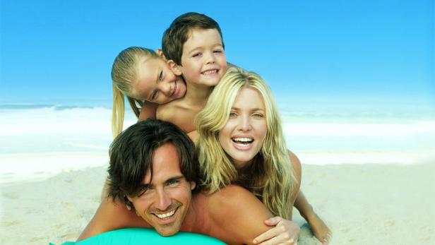 Eine glückliche Familie liegt am Strand übereinander gestapelt.