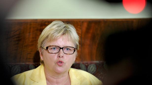 Eine Frau mit blonden Haaren und Brille spricht.