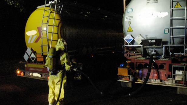 Eine Person in Schutzanzug und Atemschutzgerät hantiert an einem Tanklastwagen.