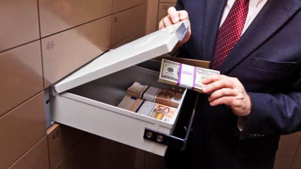 Ein Mann öffnet ein Bankschließfach gefüllt mit Bündeln von Euro- und Dollar-Scheinen.
