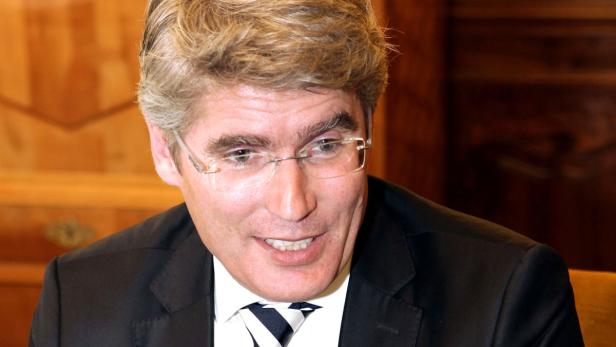 Ein Mann mit Brille, Anzug und Krawatte lächelt.