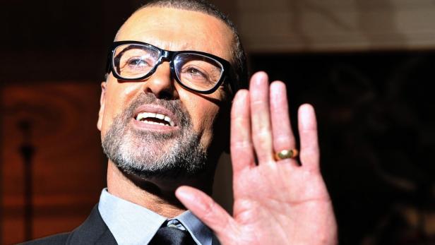 George Michael mit Brille hebt die Hand.