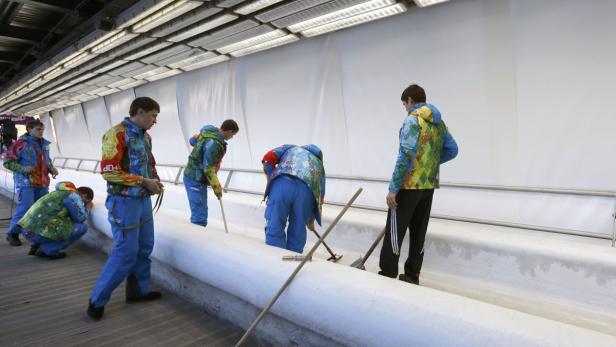 Mehrere Personen präparieren eine Eisbahn mit Werkzeugen.