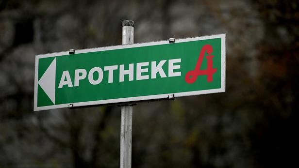Ein grünes Schild mit der Aufschrift „Apotheke“ und einem roten A mit Äskulapstab zeigt nach links.
