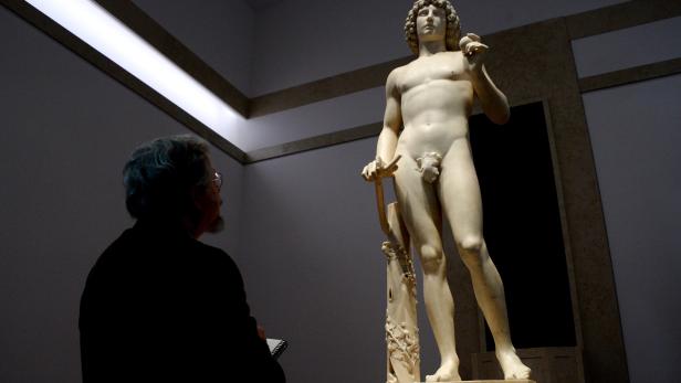 Ein Mann betrachtet eine Statue von Adam im Museum.