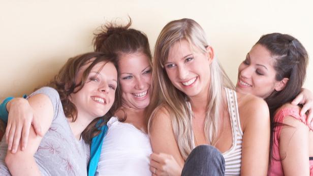 Vier junge Frauen kuscheln und lachen zusammen.