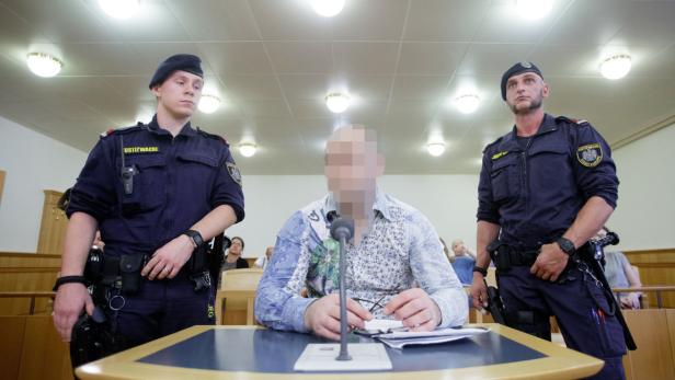 Ein Mann mit verpixelten Gesicht sitzt in einem Gerichtssaal, bewacht von zwei Justizbeamten.