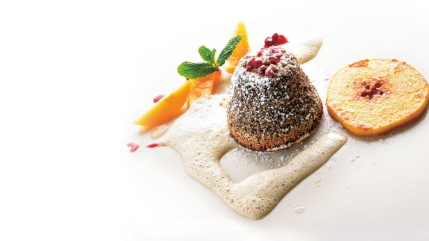 Ein Schokoladenküchlein mit Puderzucker, garniert mit Orange und Schaum.