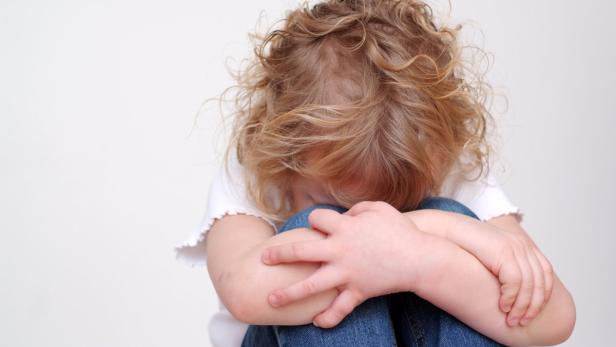 Ein Kind mit blonden Locken sitzt traurig mit dem Kopf auf den Knien.