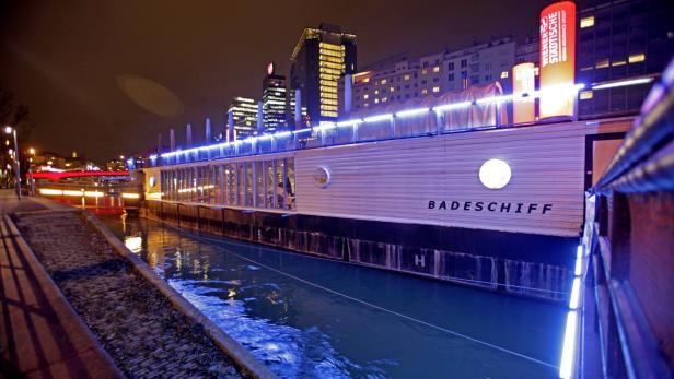 Das Badeschiff in Wien liegt nachts hell erleuchtet im Donaukanal.