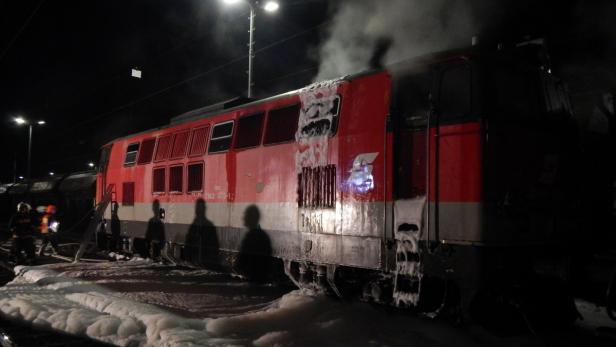 Ein roter Zug steht nachts, teilweise mit Schaum bedeckt, möglicherweise nach einem Brand.