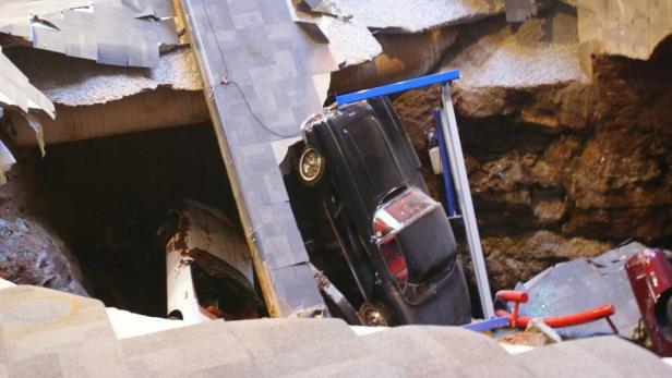 Ein schwarzes Auto ist in ein Loch gestürzt, umgeben von Trümmern und Erde.