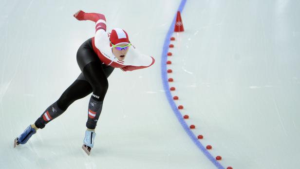 Eine Eisschnellläuferin in rot-weißer Kleidung auf einer Eisbahn.