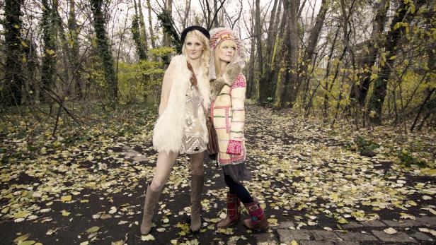 Zwei Frauen in auffälliger Kleidung posieren in einem herbstlichen Wald.