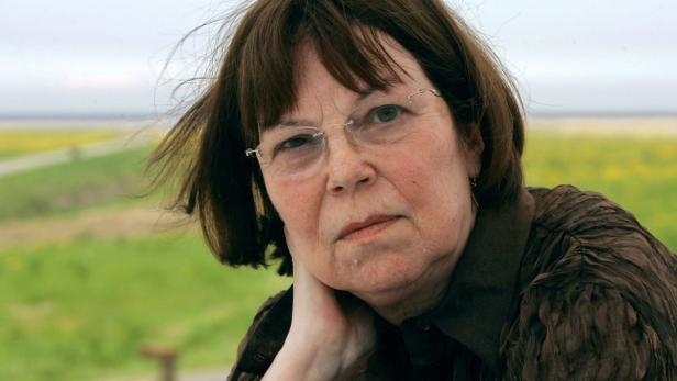 Eine Frau mit Brille und braunem Haar posiert vor einer Landschaft.