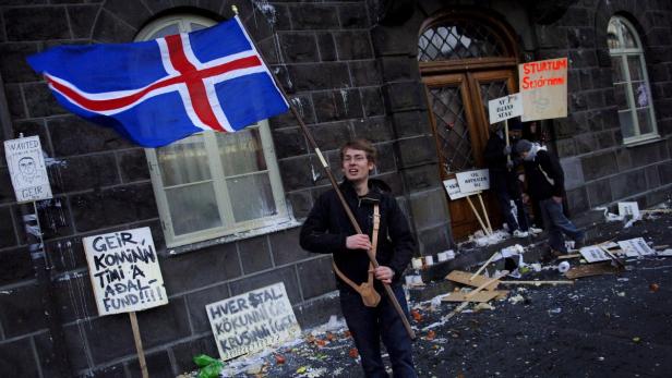 Ein junger Mann hält eine isländische Flagge vor einem Gebäude während einer Demonstration.