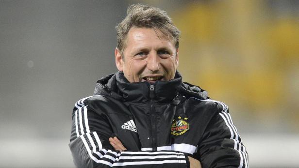 Ein Mann in einer Adidas-Jacke mit dem Logo von Rapid Wien steht mit verschränkten Armen da.
