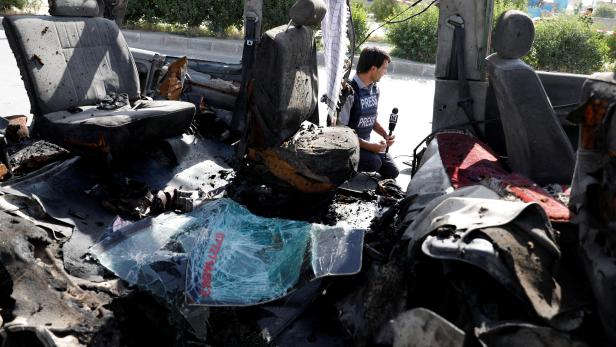 Afghan journalist reports next to a damaged van after a blast in Kabul